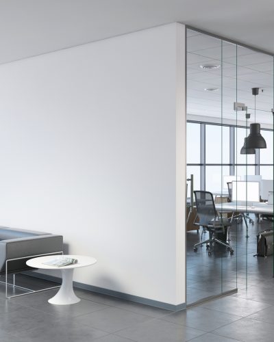 Interior view of a modern office, business template. Left side of the picture is large sofa with a plant and coffee table. Blank wall for copy space. On the right, many office desks with pendant lights above. large windows. gray floor tiles, white walls. Render